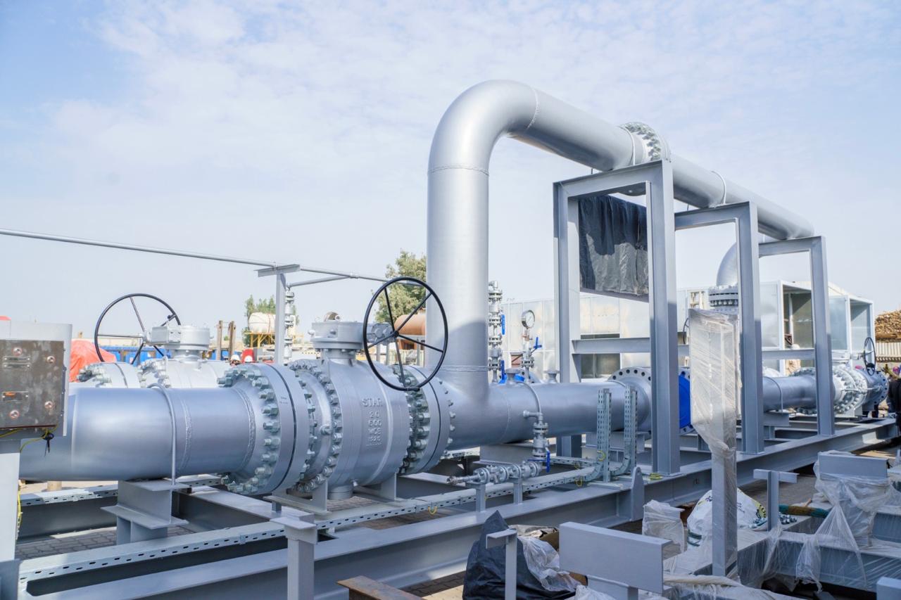 Oil field infrastructure with steel frameworks and construction equipment in a dusty outdoor environment